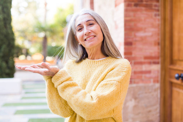 senior retired pretty white hair woman smiling, feeling confident, successful and happy, showing concept or idea on copy space on the side - Foto, imagen