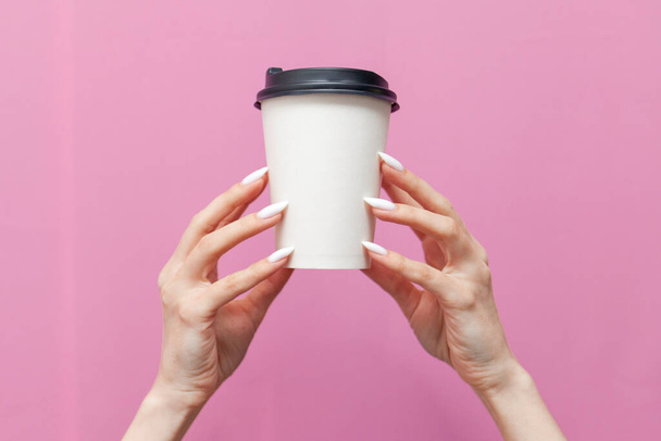 white blank paper cup of coffee in the hands of woman on pink isolated background, the girl's hands hold disposable cardboard cup with drink and advertise copy space - Foto, Imagem