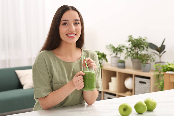 Beautiful young woman with mason jar of delicious smoothie and apples at home - Foto, immagini