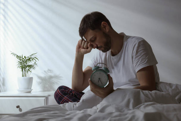 Sleepy man with alarm clock in bed at home - Φωτογραφία, εικόνα