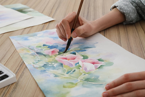 Woman painting flowers with watercolor at wooden table, closeup. Creative artwork - Foto, Imagem