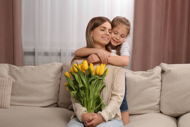 Little daughter congratulating mom with bouquet of yellow tulips at home. Happy Mother's Day - Foto, imagen