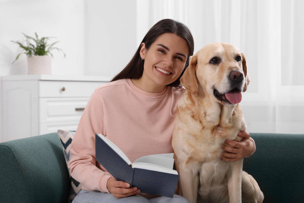 Happy woman sitting with cute Labrador Retriever on sofa at home - Foto, Imagen