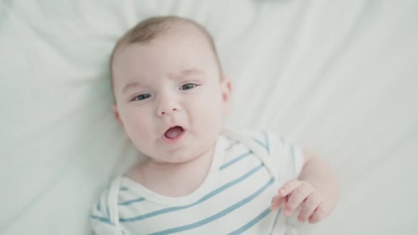 Schattige blanke baby liggend op bed met ontspannen uitdrukking in de slaapkamer - Video