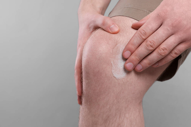 Man applying ointment onto his knee on light grey background, closeup. Space for text - Fotografie, Obrázek