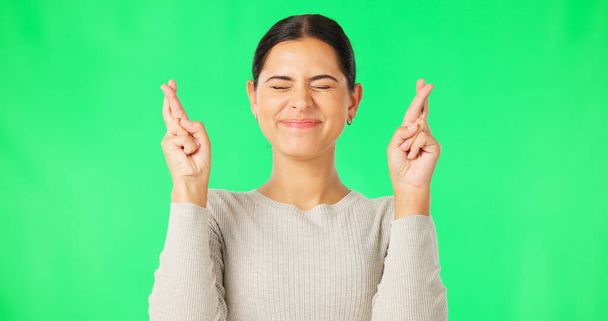 Excited woman, fingers crossed and face on green screen, background and studio for good luck. Portrait of happy female model hope for winning prize, wish and optimism with emoji sign, hands and smile. - Fotó, kép