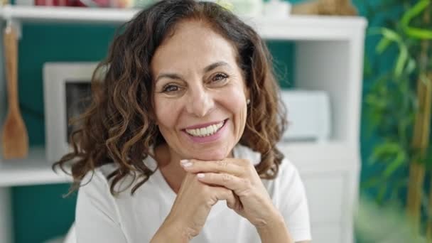 Keski-ikä latino nainen hymyilee luottavainen istuu pöydällä ruokailuhuoneessa - Materiaali, video