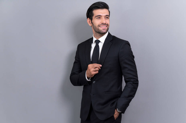 Stylish businessman in black suit posing confidently on isolated background, with a happy and optimistic smile as success and professionalism for businessman. Fervent - 写真・画像