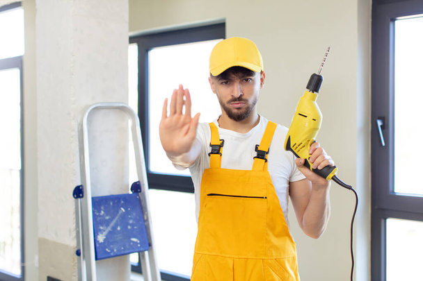 young handsome man looking serious showing open palm making stop gesture. handyman and drill concept - Photo, Image