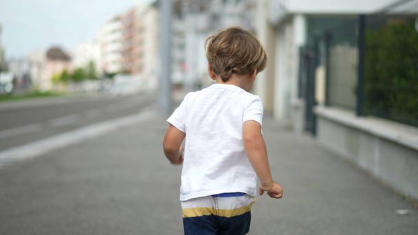 Back of happy kid walking outside in city street. Child standing in urban sidewalk - Photo, Image