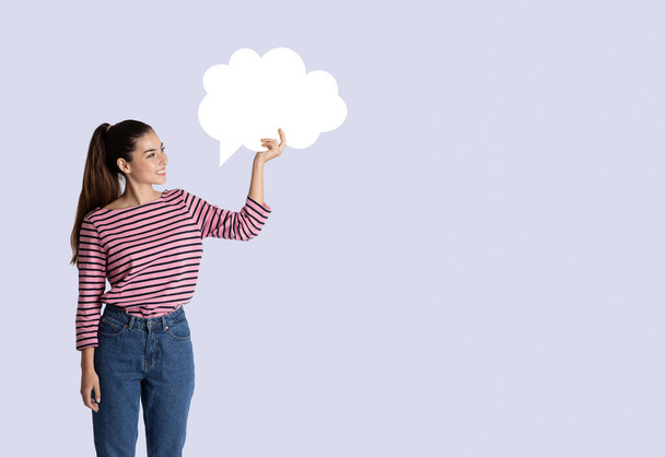 Mujer joven bastante hispana feliz en traje casual sosteniendo burbuja conversación en blanco sobre su cabeza en fondo gris estudio, espacio libre en blanco para el diseño, concepto de comunicación - Foto, imagen