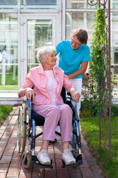 Vanhempi nainen pyörätuolissa hoitoavustajan kanssa
 - Valokuva, kuva