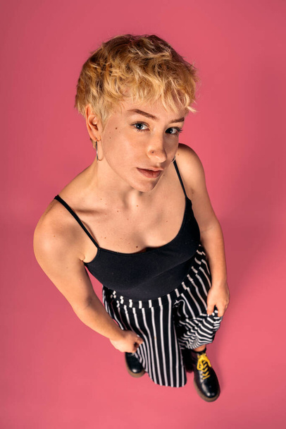 Stock photo of expressive girl wearing black tank top standing and looking at camera over pink background. - Foto, imagen