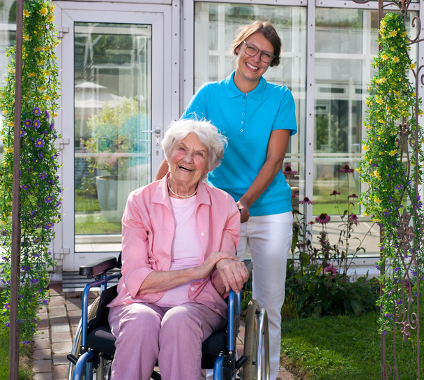 Tekerlekli sandalyeye mahkum bakım asistanı ile yaşlı bayan - Fotoğraf, Görsel