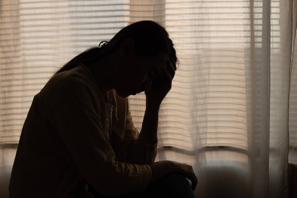 Female having depression sitting alone in bedroom dark corner. woman headache unhappy emotion. young anxiety despairing mental health problems. Dark Tone. - Фото, изображение