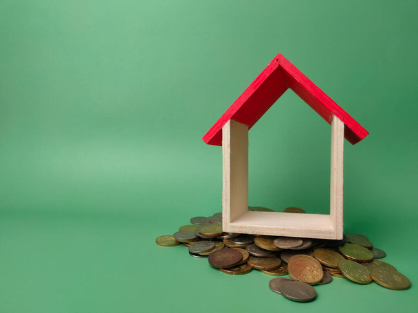 Wooden house on a scattering of coins on a green background. - Photo, Image