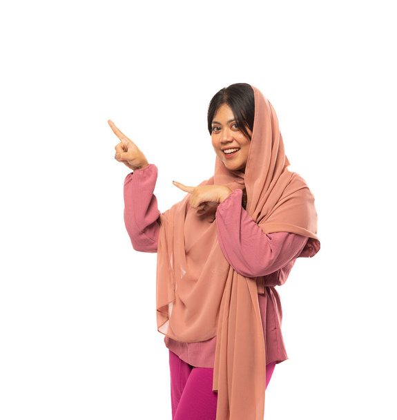 Asian veiled woman with fingers showing something in an isolated background with copyspace - Foto, Imagem