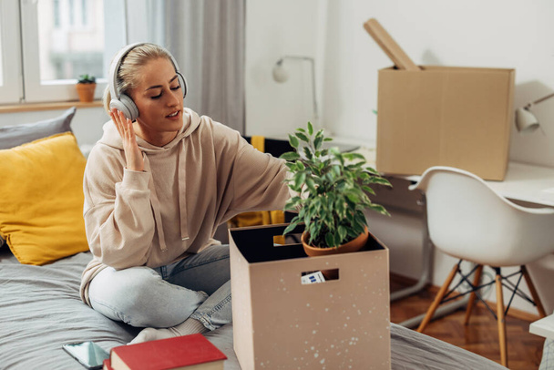 A young Caucasian woman is unpacking her things from a box while listening to music - Photo, Image