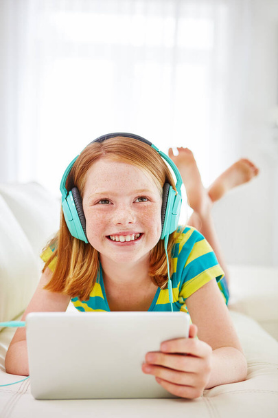 Aufwachsen in einer vernetzten Welt. ein kleines Mädchen mit einem digitalen Tablet mit Kopfhörer zu Hause - Foto, Bild