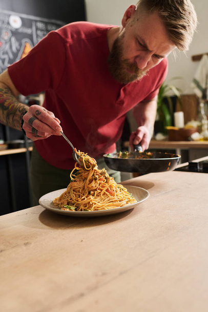 Modern kaukázusi ételblogger áll a tetőtéri konyhában forró tésztát szolgálva fel serpenyőtől tányérig. - Fotó, kép