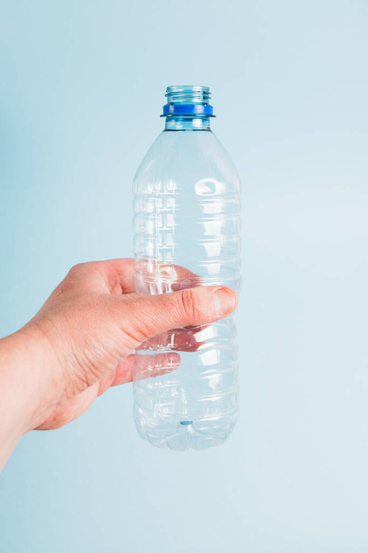 Used plastic bottle in human hand on blue paper background. Concept of earth day, zero waste and plastic recycling - 写真・画像