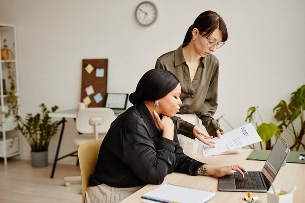 Seitenansicht Porträt zweier erfolgreicher Geschäftsfrauen, die im Minimal Office über Arbeitsunterlagen diskutieren - Foto, Bild