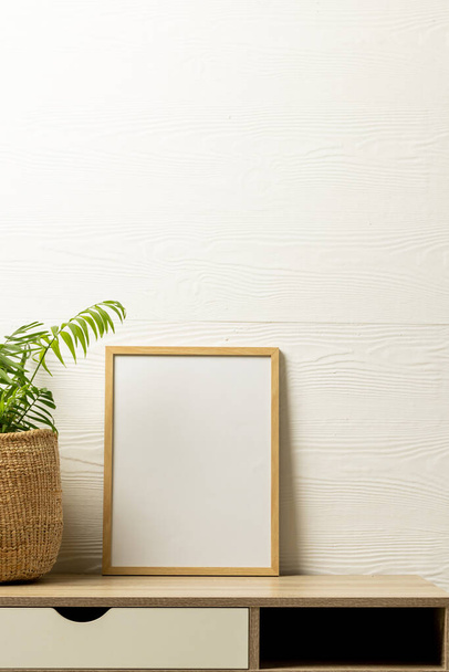 Vertical of empty wooden frame with copy space and plant in pot on desk against white wall. Mock up frame template, interior design and decoration. - Foto, Imagem