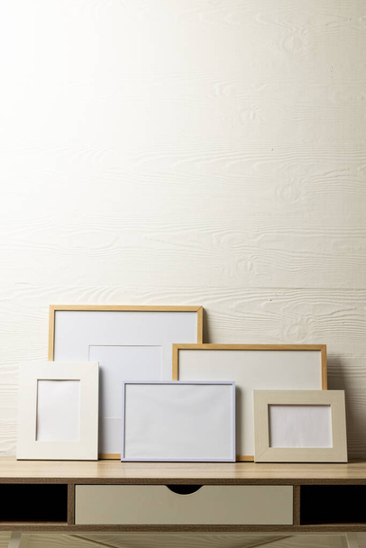 Vertical of five various empty frames with copy space on table against white wall. Mock up frame template, interior design and decoration. - Foto, imagen
