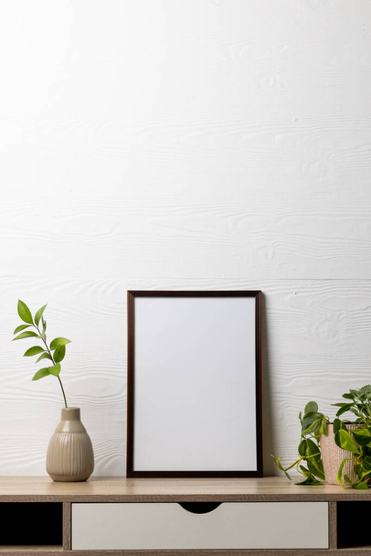 Vertical of black empty frame with copy space and plants in pots on table against white wall. Mock up frame template, interior design and decoration. - Φωτογραφία, εικόνα