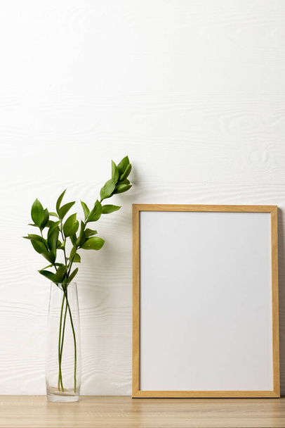 Vertical of empty wooden frame with copy space and plant on table against white wall. Mock up frame template, interior design and decoration. - Фото, зображення