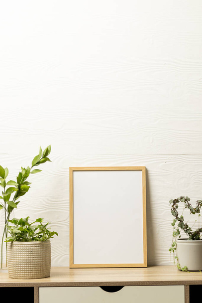 Vertical of empty wooden frame with copy space and plants in pots on desk against white wall. Mock up frame template, interior design and decoration. - Foto, afbeelding