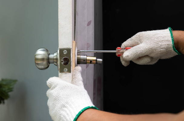 Locksmith on wood door with screwdriver for repair or fix silver knob. - 写真・画像