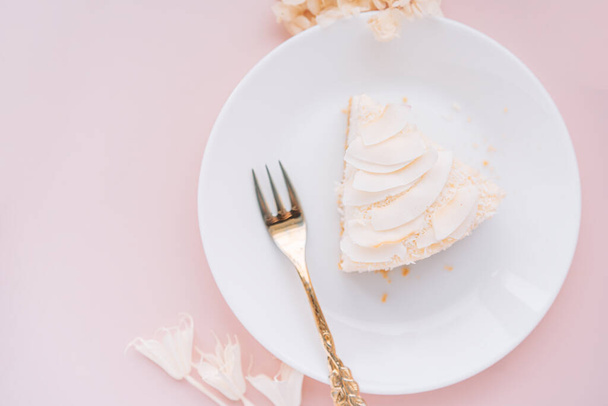 ピンクの背景にフォークでプレート上のココナッツ風味の白いチーズケーキ. - 写真・画像