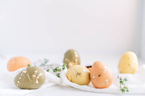 Huevos de Pascua de diferentes colores en servilletas blancas con flores secas. - Foto, Imagen