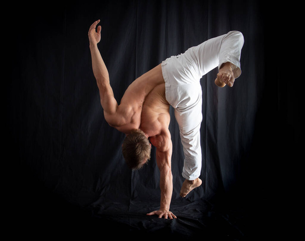 circus artist keeps balance on one hand isolated on a black background. concept of handstand and calisthenic. - Fotó, kép