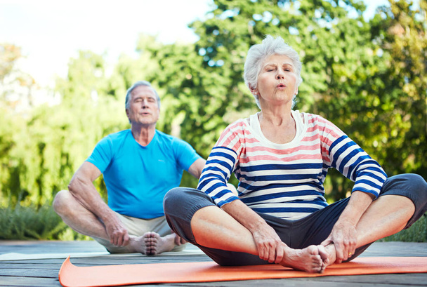 Find that zen. a senior couple doing yoga together outdoors - Foto, afbeelding