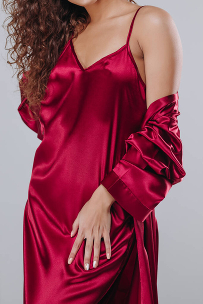 very sexy curly girl in a red robe, night dress on a gray background. home clothes concept. catalog photo - Photo, Image