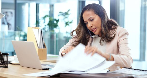 Female advertising agent looking busy while talking on a phone call and searching through documents on a messy table in an office. Female marketing professional trying to find an important form. - Photo, image