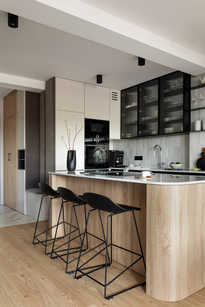 Modern composition of kitchen space with design kitchen island, black hookers, grey table, flowers, furnitures, and elegant personal accessories. Stylish home decor. Template. - Foto, afbeelding