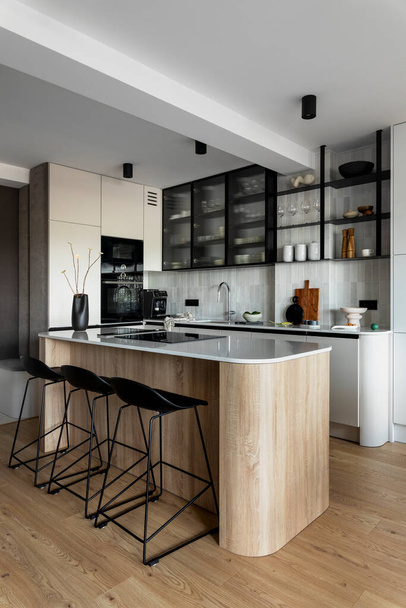 Modern composition of kitchen space with design kitchen island, black hookers, grey table, flowers, furnitures, big window and elegant personal accessories. Stylish home decor. Template. - 写真・画像