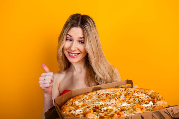 Une belle jeune fille blonde en forme avec une grande boîte à pizza ouverte. Isolé sur jaune. - Photo, image