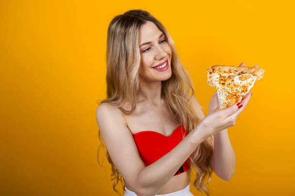 Güzel, formda, sarışın bir kız pizza dilimiyle poz veriyor. Sarıda izole edilmiş.. - Fotoğraf, Görsel
