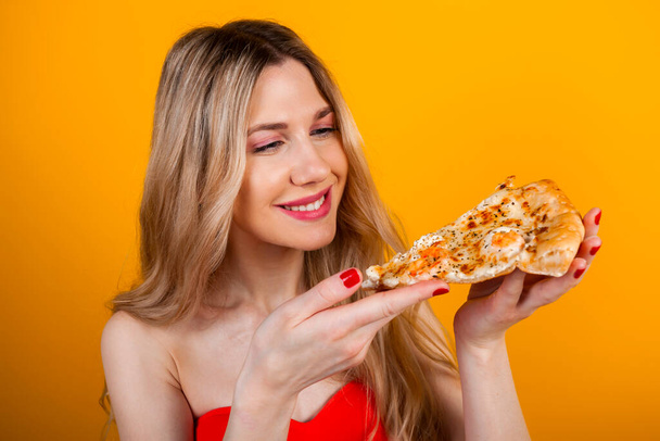 Ein schönes, fittes, junges blondes Mädchen posiert mit einer Pizzascheibe. Isoliert auf Gelb. - Foto, Bild