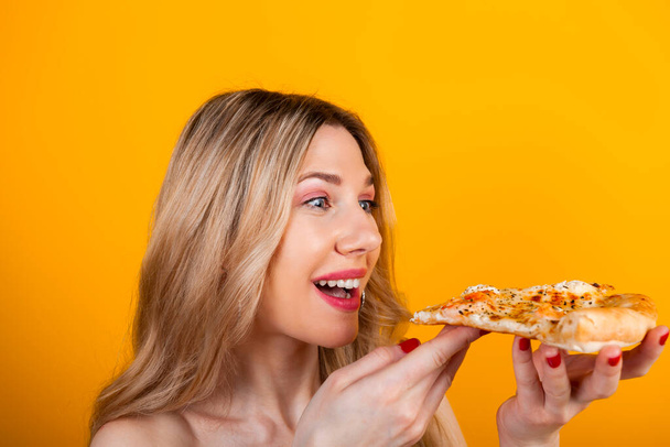 Красива підходить молода блондинка позує зі скибочкою піци. Ізольовані на жовтому
. - Фото, зображення