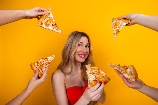 Una hermosa chica rubia sensual en forma rodeada de manos con rebanadas de pizza a su alrededor. Aislado sobre amarillo. - Foto, imagen