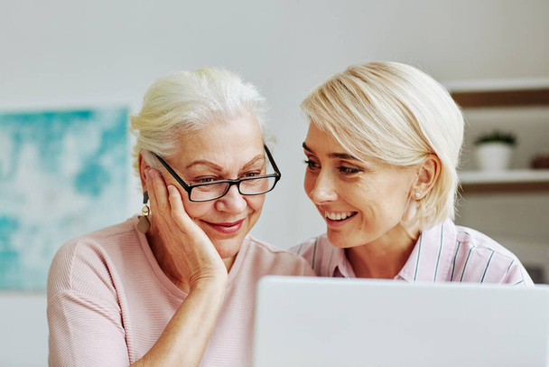 Close up portrait of smiling young woman with senior mother using laptop together at home and shopping online - Photo, Image