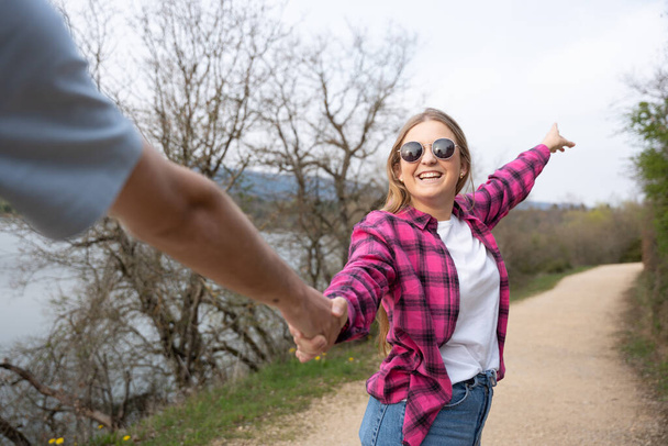 Fiatal nő mutatja meg a helyes irányt a barátjának, miközben fogja a kezét a természetben. Tini sétál kavicsos ösvényen. - Fotó, kép