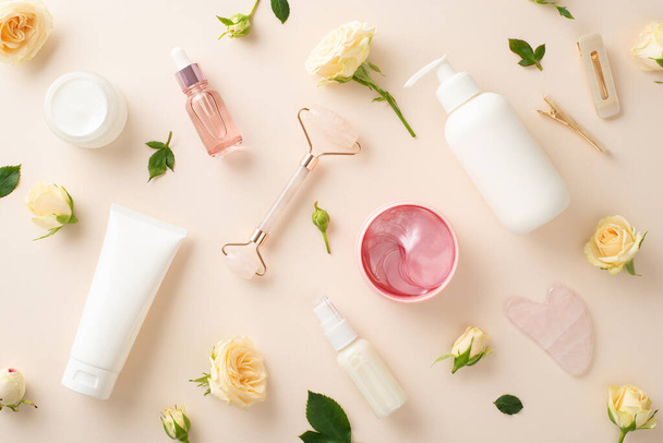 Trendy huidverzorging concept. Een bovenaanzicht van pomp flessen, serum, en massage gezicht rollen omgeven door prachtige rozen op een pastel beige achtergrond - Foto, afbeelding