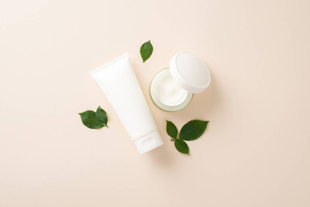 Élevez votre jeu de beauté avec le concept de cosmétologie des soins de la peau, présentant des flacons pompe de crème visage aux côtés de feuilles vertes sur un fond beige pastel - Photo, image