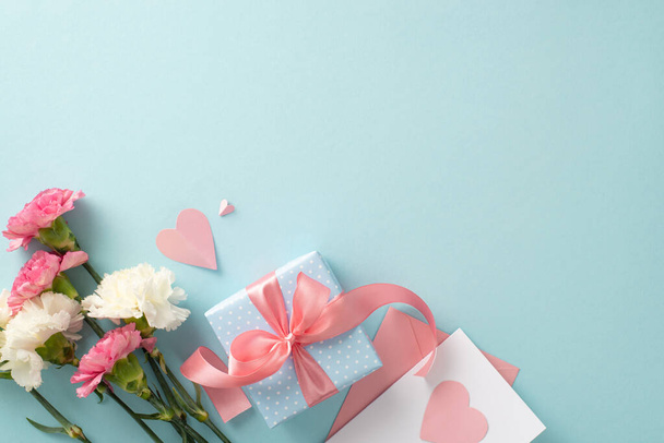 Mother's Day celebration concept. Top view flat lay photo of gift boxes with pink ribbons, carnation flowers, and pink paper hearts on pastel blue background with empty space for text or advert - Foto, imagen